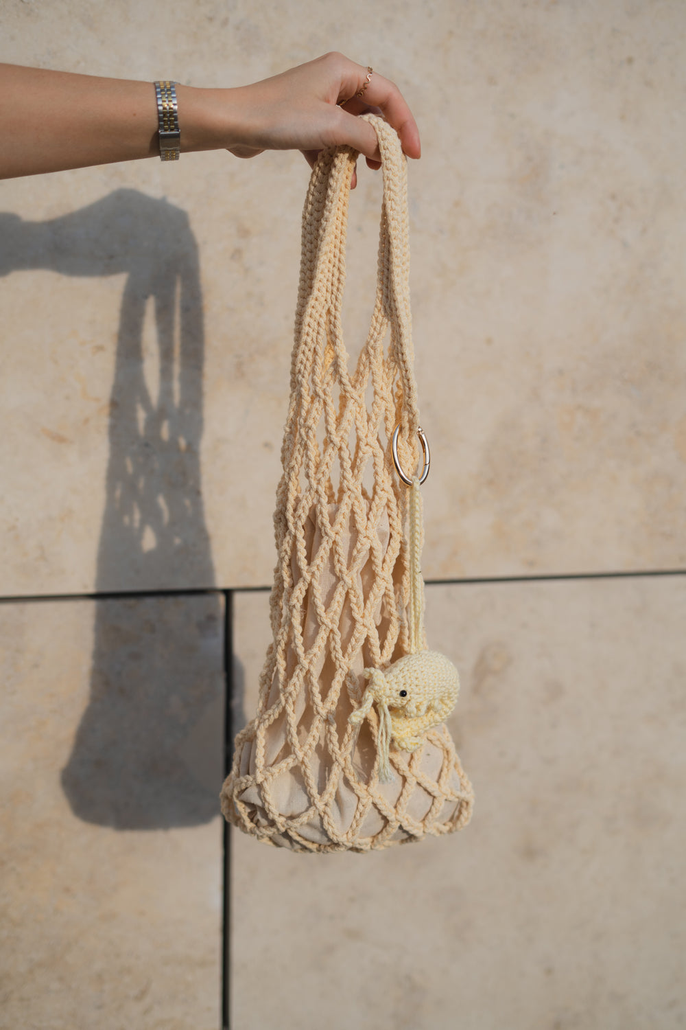 Ręka trzymająca torebkę dzierganą na szydełku z brelokiem krewetka w odcieniu masełkowym Sirka handmade