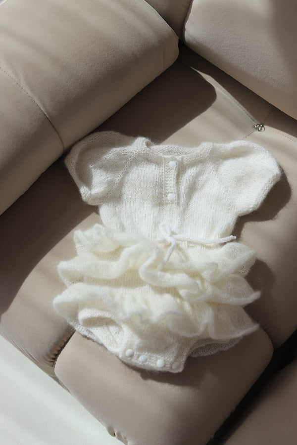 Dziecięca sukieneczka ręcznie robiona  w odcieniu białym z falbankami Sirka handmade leżaca na kanapie