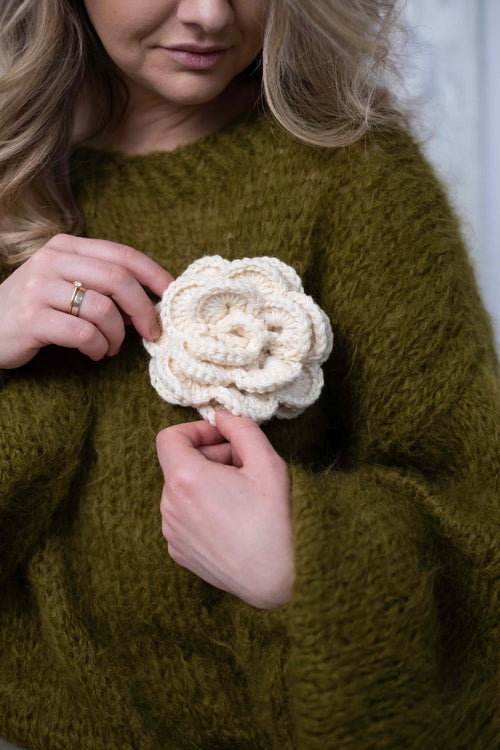 Kobieta w oliwkowym swetrze trzymająca broszkę kwiatek Sirka handmade