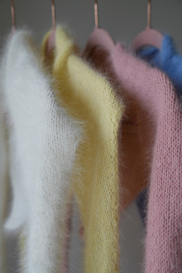 Chusty z angory i wełny merino Sirka handmade wiszące na wieszakach w odcieniach od lewej biały, masełkowy, różowy, niebieski
