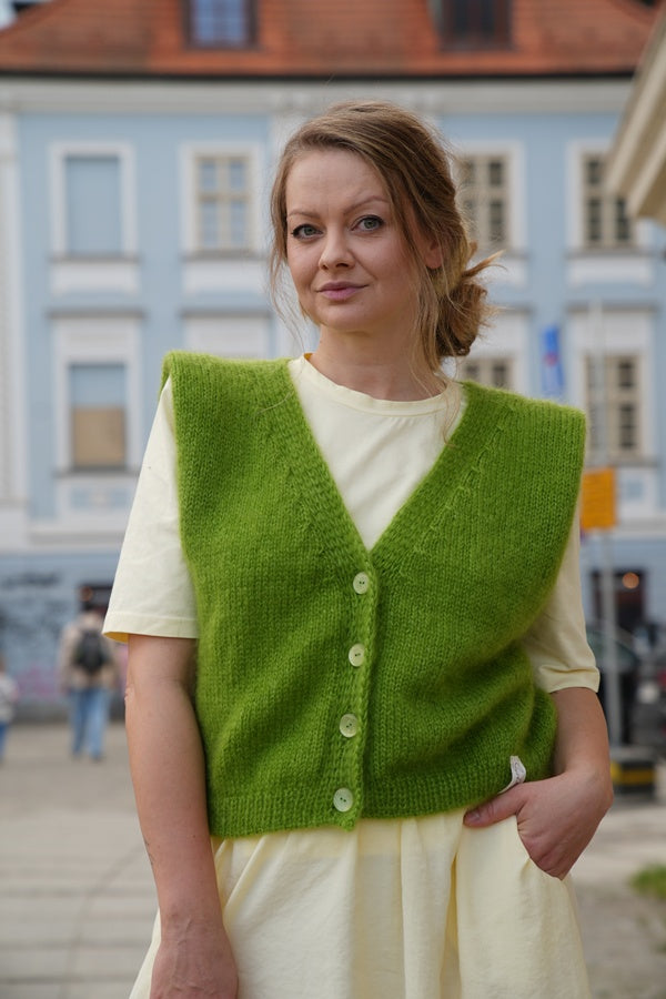 Uśmiechnięta kobieta w kamizelce w odcieniu zieleni Sirka handmade na tle miasta