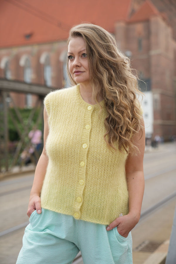 Kobieta patrząca w bok w żółtej kamizelce Sirka handmade na tle miasta