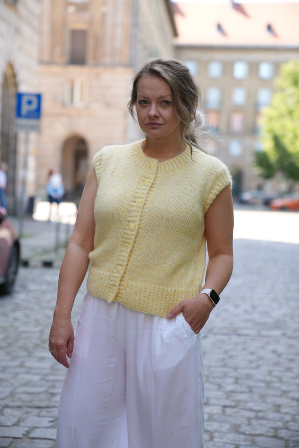 Kobieta w kamizelce z wełny merino w odcieniu masełkowym Sirka handmade na tle miasta