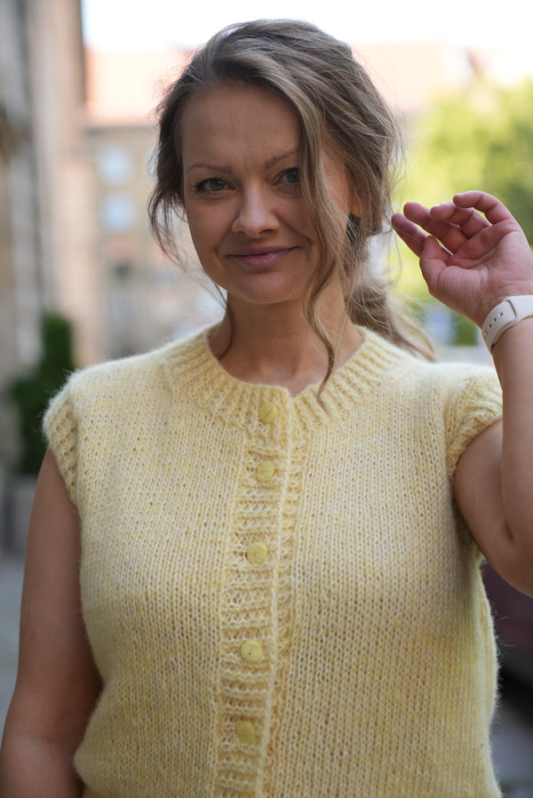 Uśmiechnięta kobieta w kamizelce z wełny merino w odcieniu masełkowym Sirka handmade na tle miasta