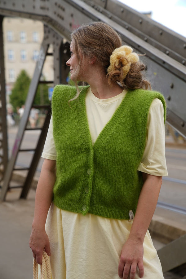 Kobieta patrząca w bok w zielonej kamizelce i sukience w kucyku spiętym żółtą gumką do włosów Sirka handmade