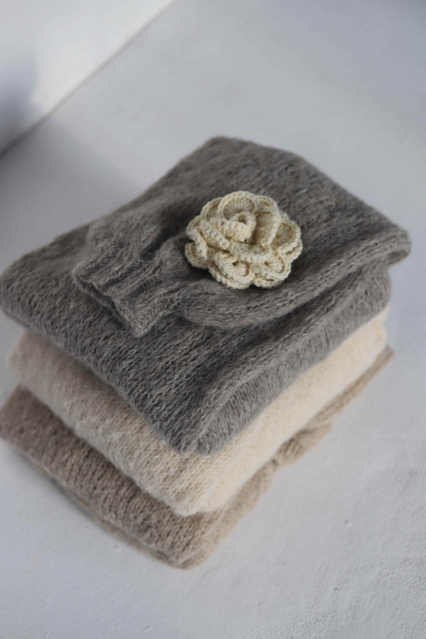 Broszka kwiatek leżąca na trzech ułożonych swetrach Sirka handmade