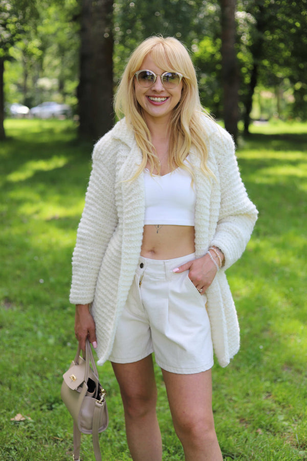 Uśmiechnięta kobieta w parku w ręcznie robionej marynarce Coco oversize z alpaki Sirka w kolorze śmietankowym