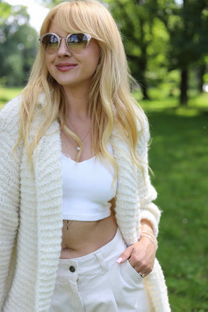 Uśmiechnięta kobieta w parku w ręcznie robionej marynarce Coco oversize z alpaki Sirka w kolorze śmietankowym