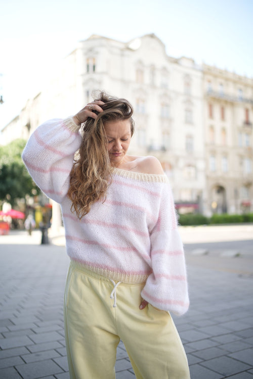 Kobieta poprawiająca włosy w swetrze z paseczkami Sirka handmade na tle miasta