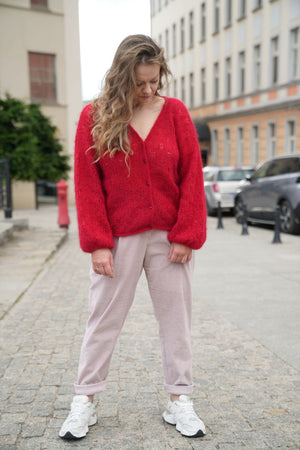 Kobieta patrząca w dół w czerwonym kardiganie SIrka handmade na tle miasta
