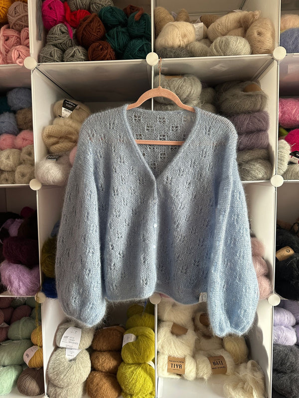 Kardigan Sirka handmade na wieszaku na tle szafki z włóczkami