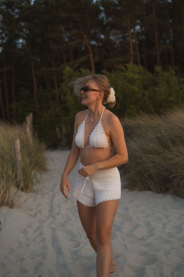 Radosna kobieta stojąca na plaży w ręcznie robionym z jedwabiu biustonoszu i szortach Sirka handmade