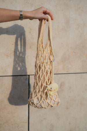 Ręka trzymająca torebkę dzierganą na szydełku z brelokiem krewetka w odcieniu masełkowym Sirka handmade