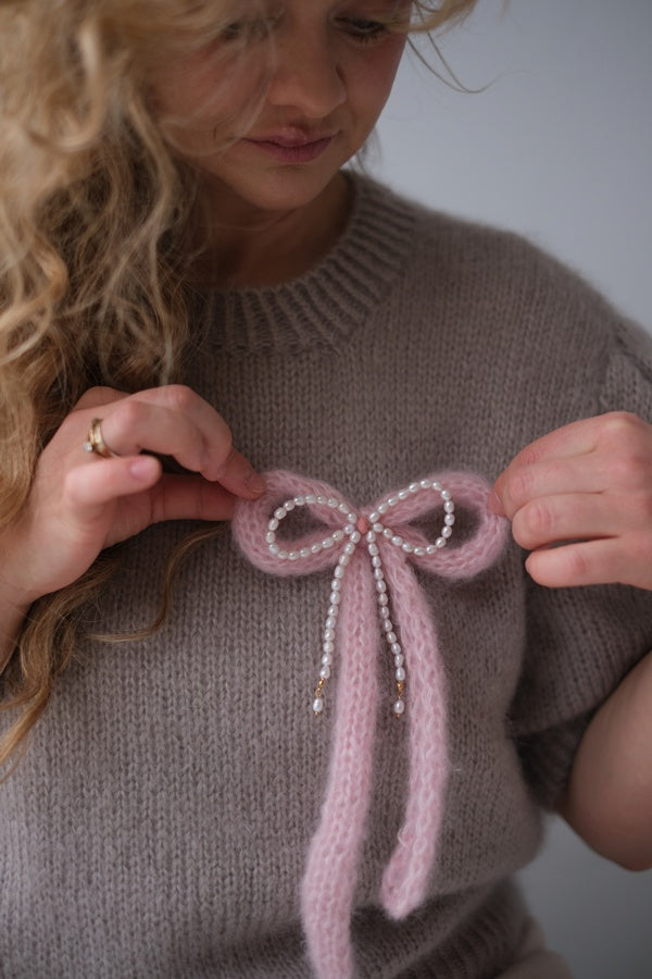 Kobieta trzymająca w dłoniach broszkę w kształcie kokardki.