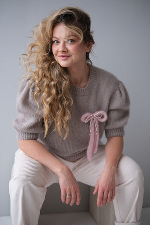 Kobieta w swetrze z broszką w kształcie kokardki z perłami.