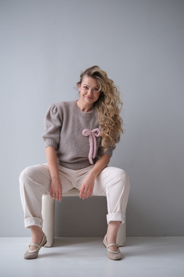 Siedząca kobieta w swetrze z broszką w kokardkę.