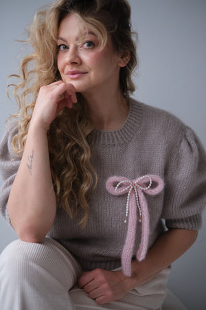 Kobieta w swetrze z broszką w kształcie kokardki z perłami.