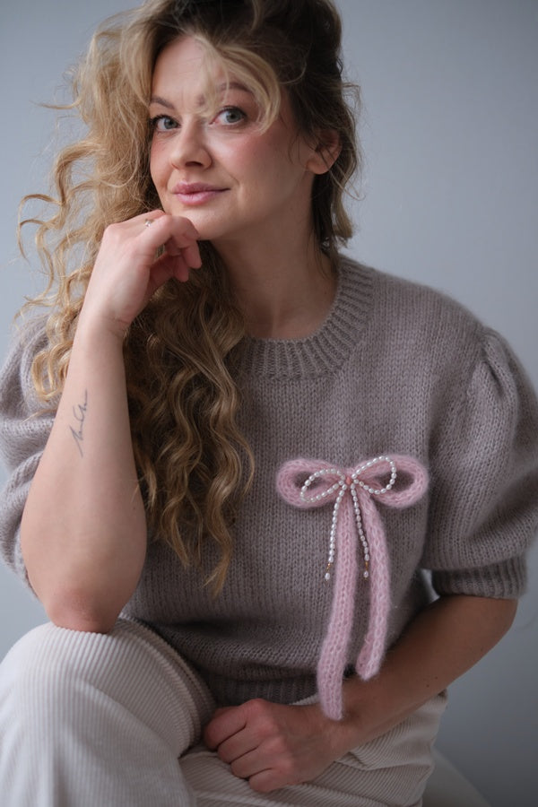 Kobieta w swetrze z broszką w kształcie kokardki z perłami.
